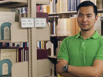 young man in library with his arms folded in front of him