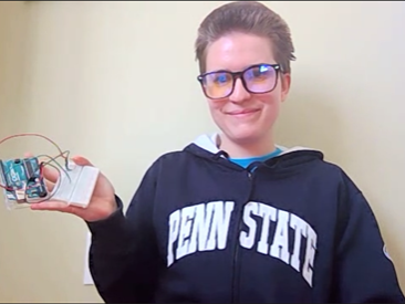 A female engineering student holds up an Arduino test kit and smiles.