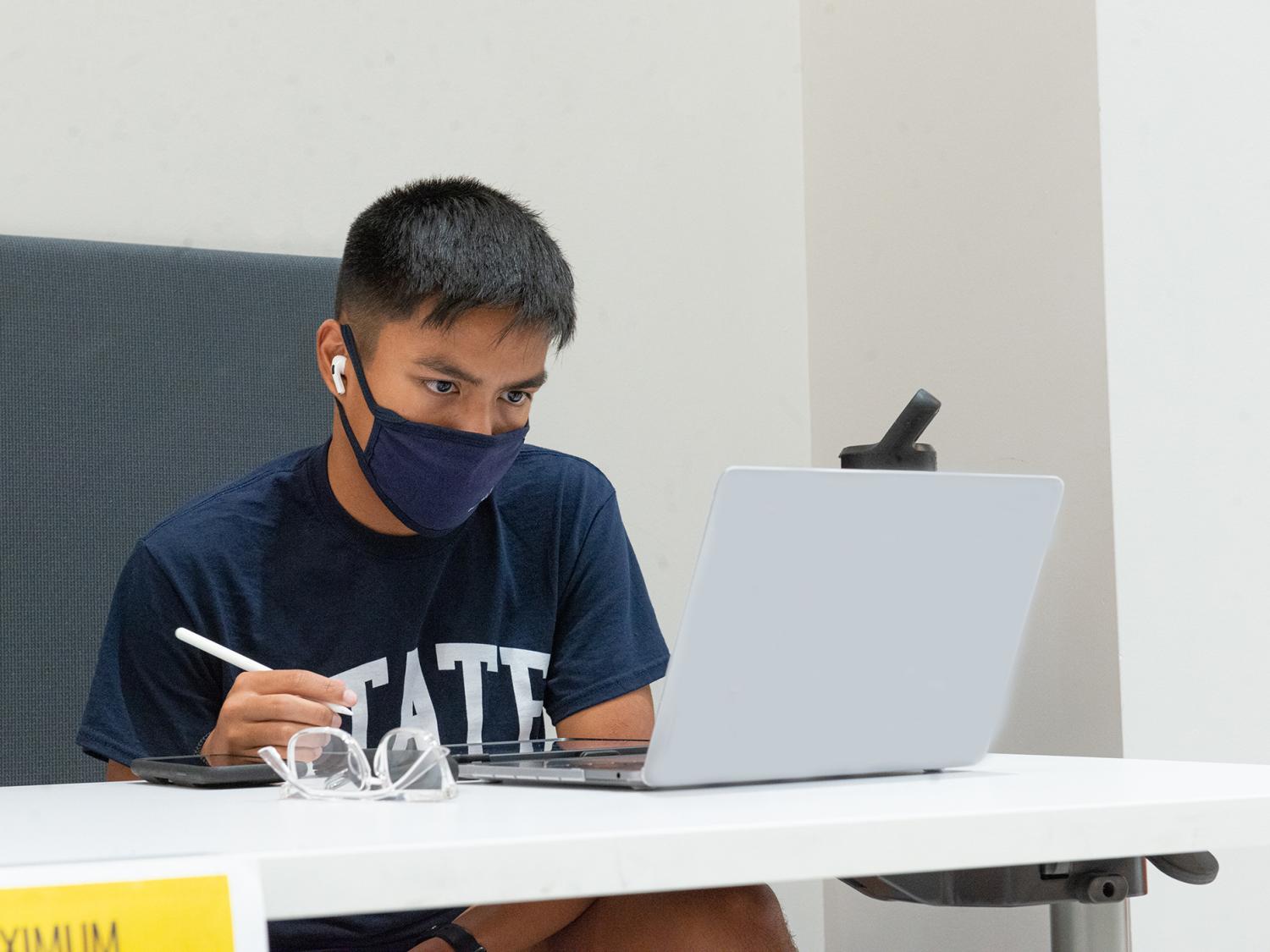 a male student in a blue t shirt working at a laptop computer