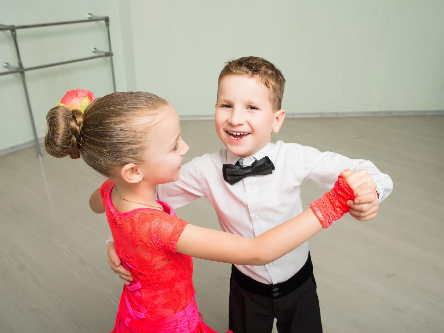 A boy and girl dressed in formalwear face each other while they dance.