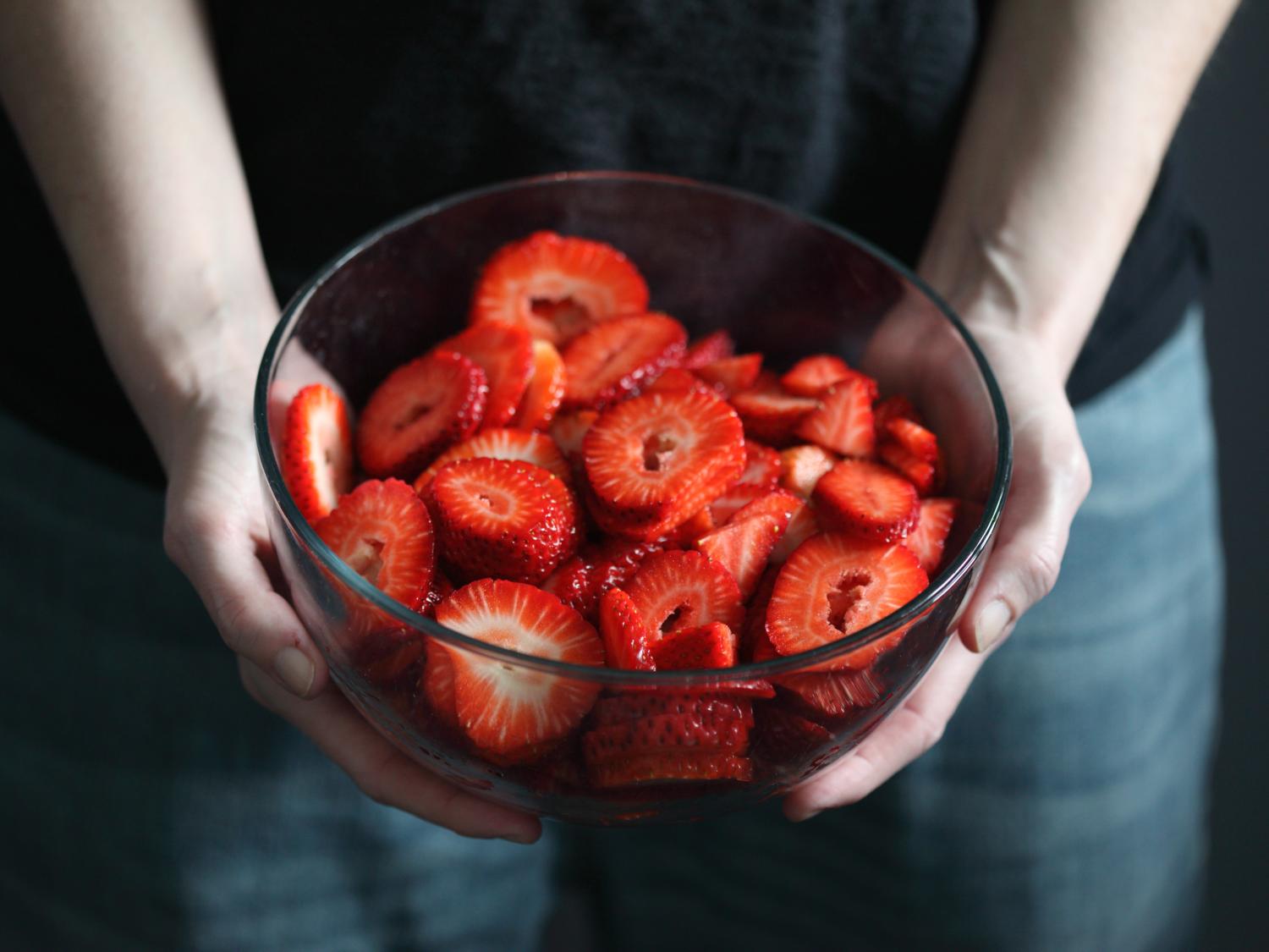Person holding bowl of cut strawberries
