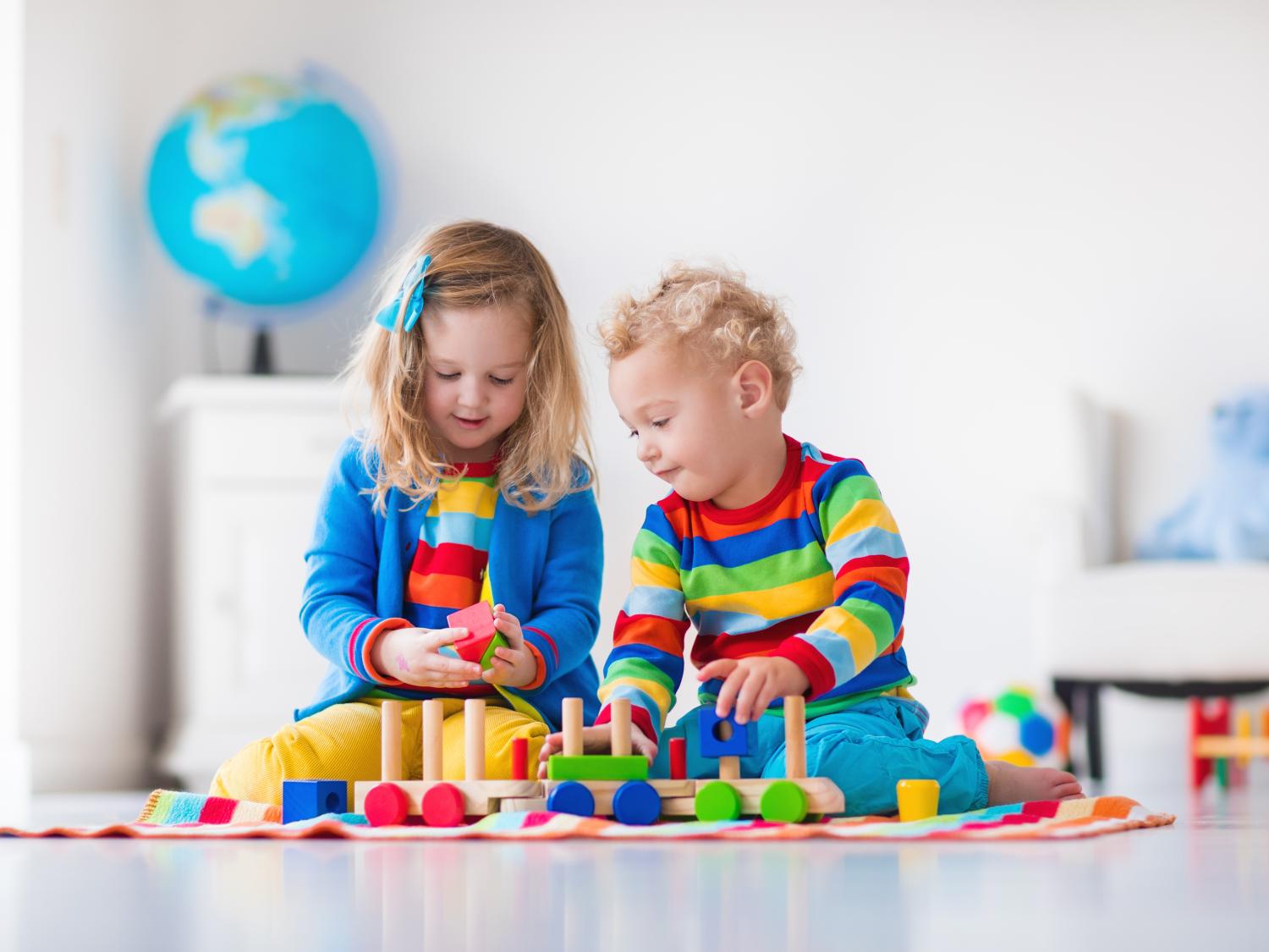 Children playing with wooden train. Toddler kid and baby play with blocks, trains and cars. Educational toys for preschool and kindergarten child. Boy and girl build toy railroad at home or daycare.