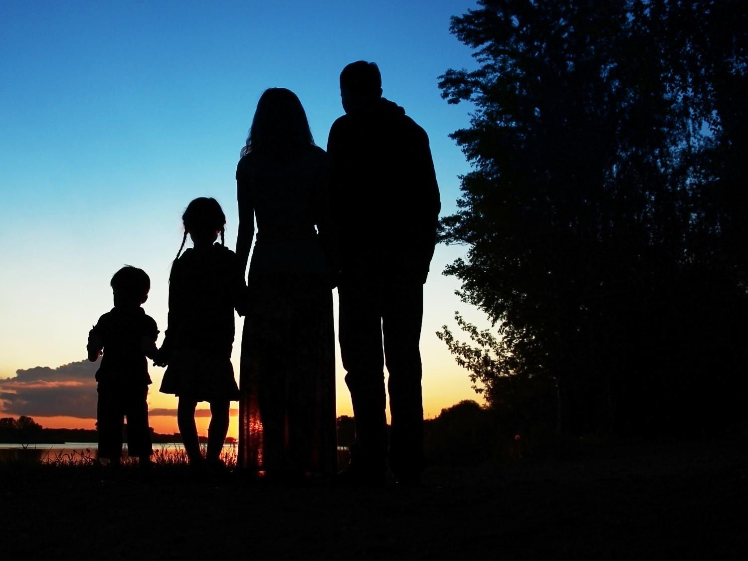 Silhouette  of family, including a father, mother and two children holding hands.