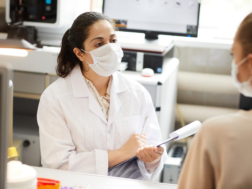A doctor wearing a paper mask has a conversation with a clinical trial participant wearing a paper mask. 