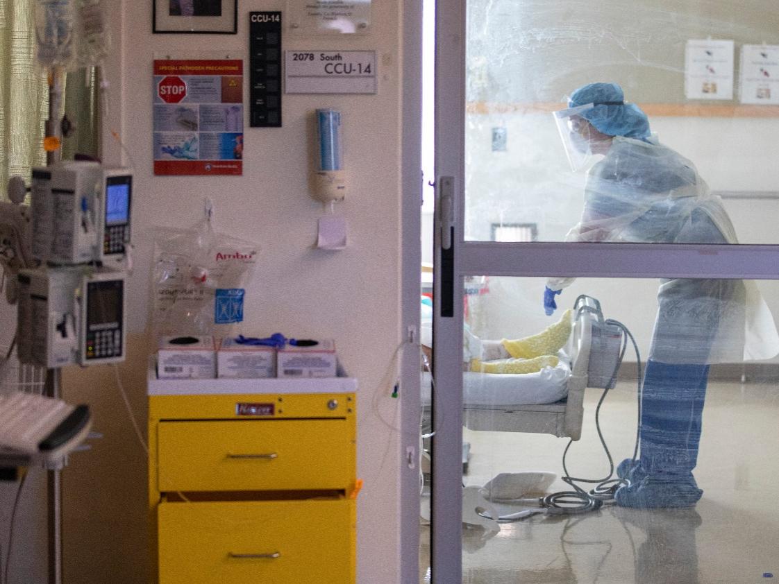 A doctor wearing PPE stands at the foot of a patient's bed in a COVID-19 unit.