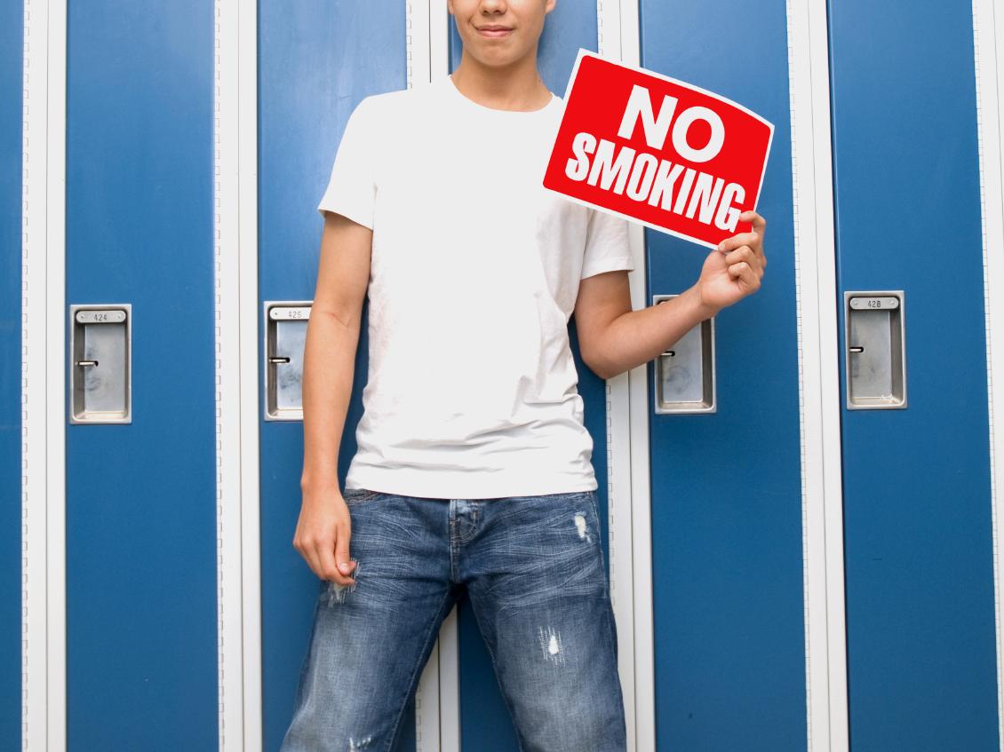 teenage boy in front of lockers, holding no smoking sign