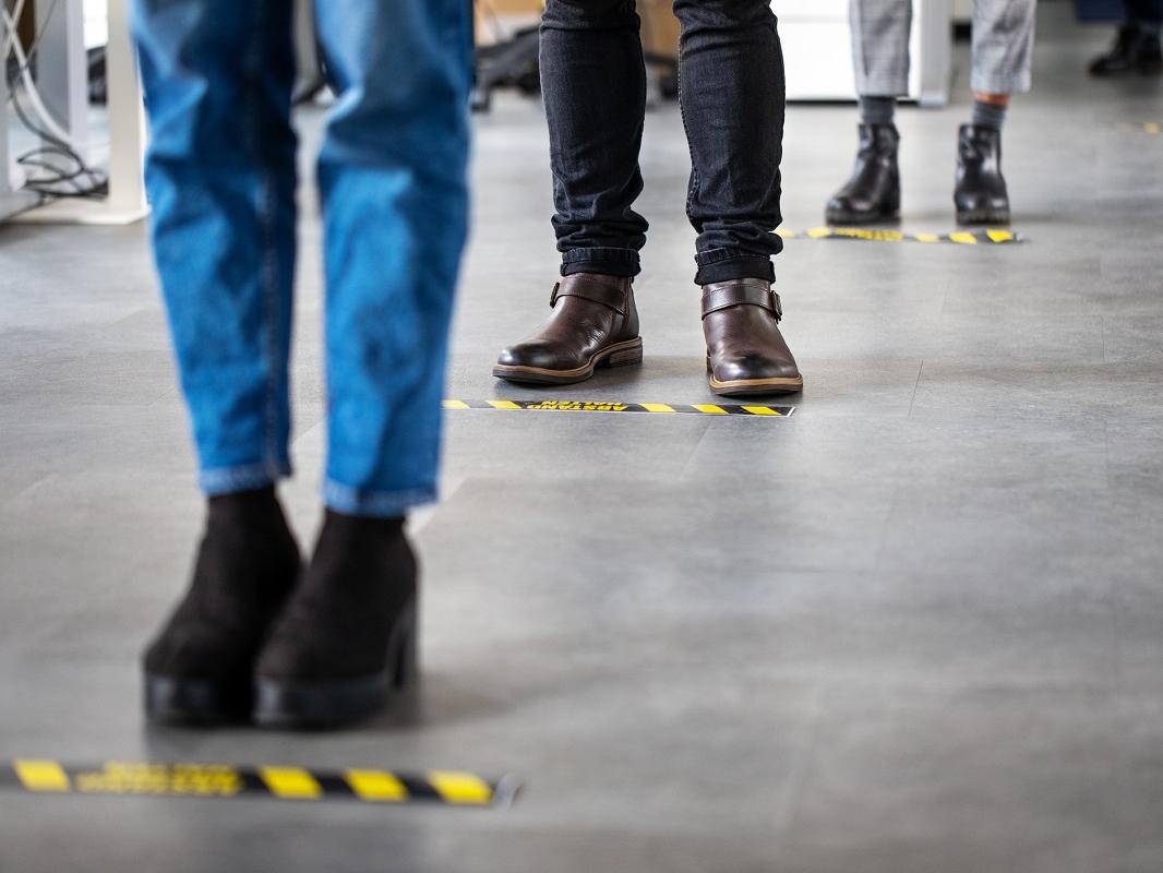 Low angle shot of business people standing behind social distancing signage on office floor. People in queue at office for safe entry checks post coronavirus pandemic.