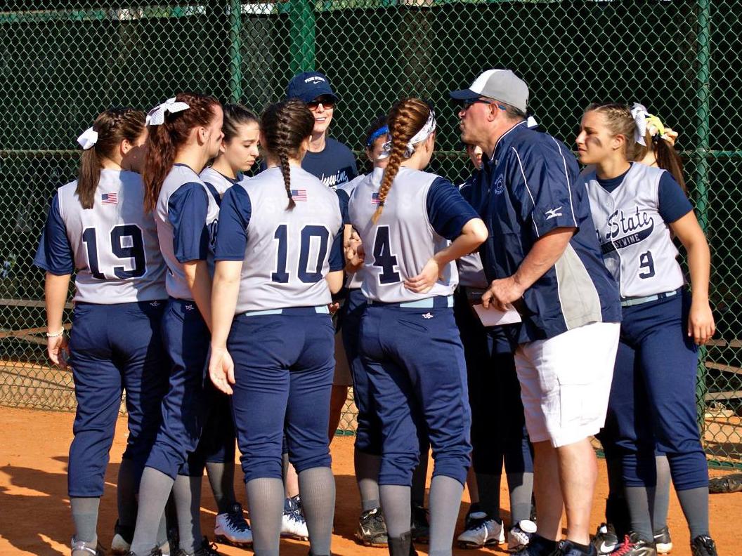 The women’s softball team huddles around Head Coach 