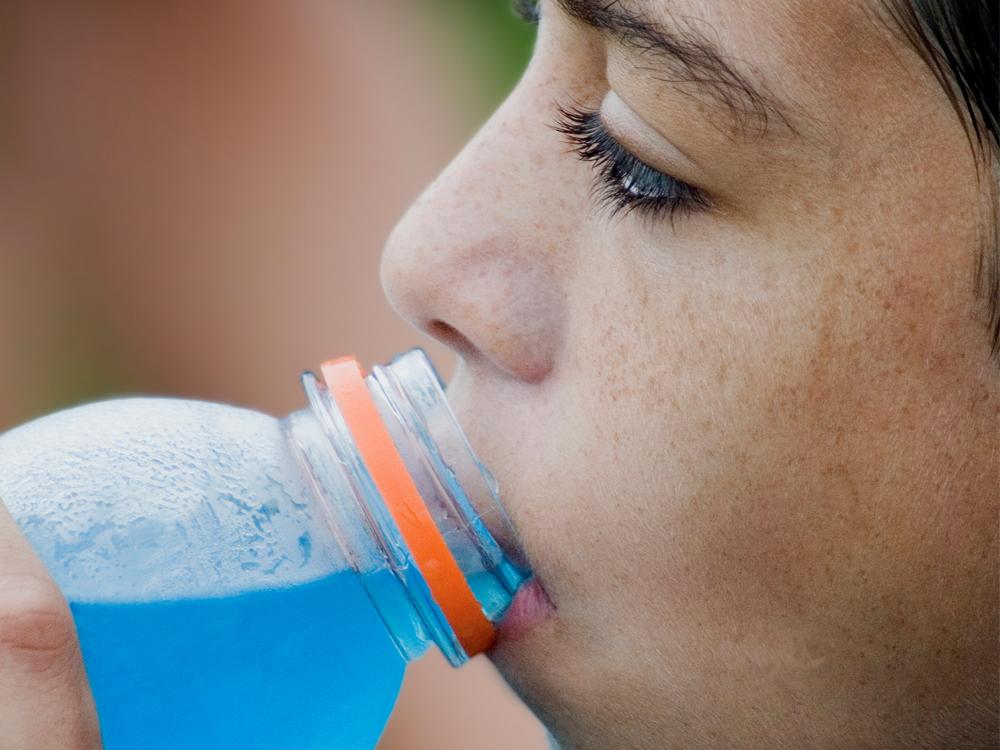 A close-up of a young girl drinking a blue sports drink.