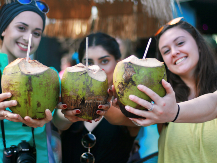Three young women holding coconut drinks