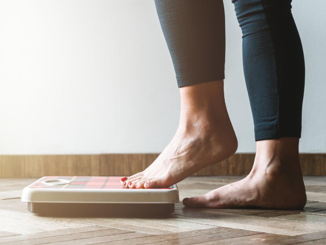 A woman steps onto a bathroom scale with her left foot first. Image is from the knees down.