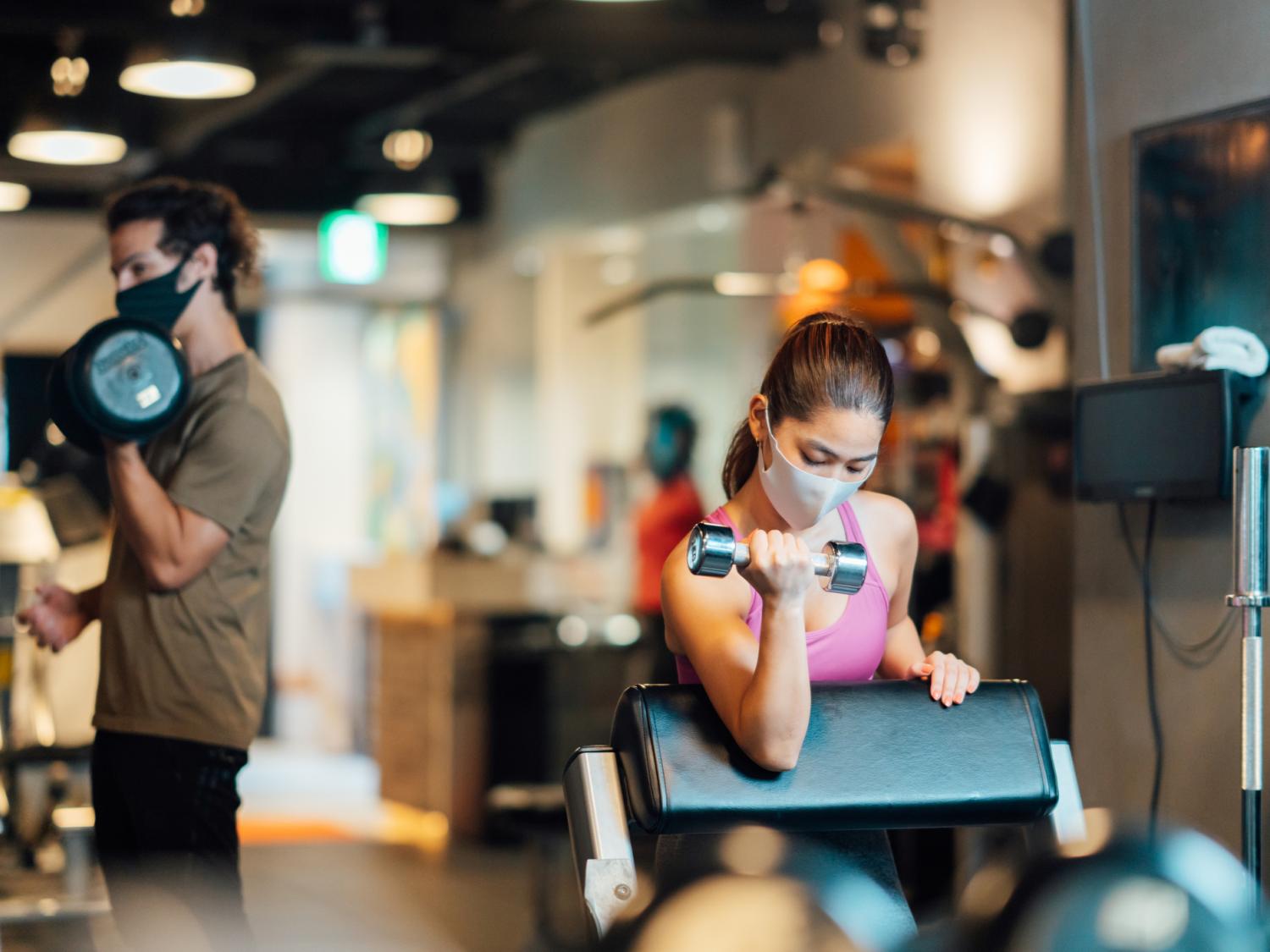 Two people wearing masks in a gym and weight training