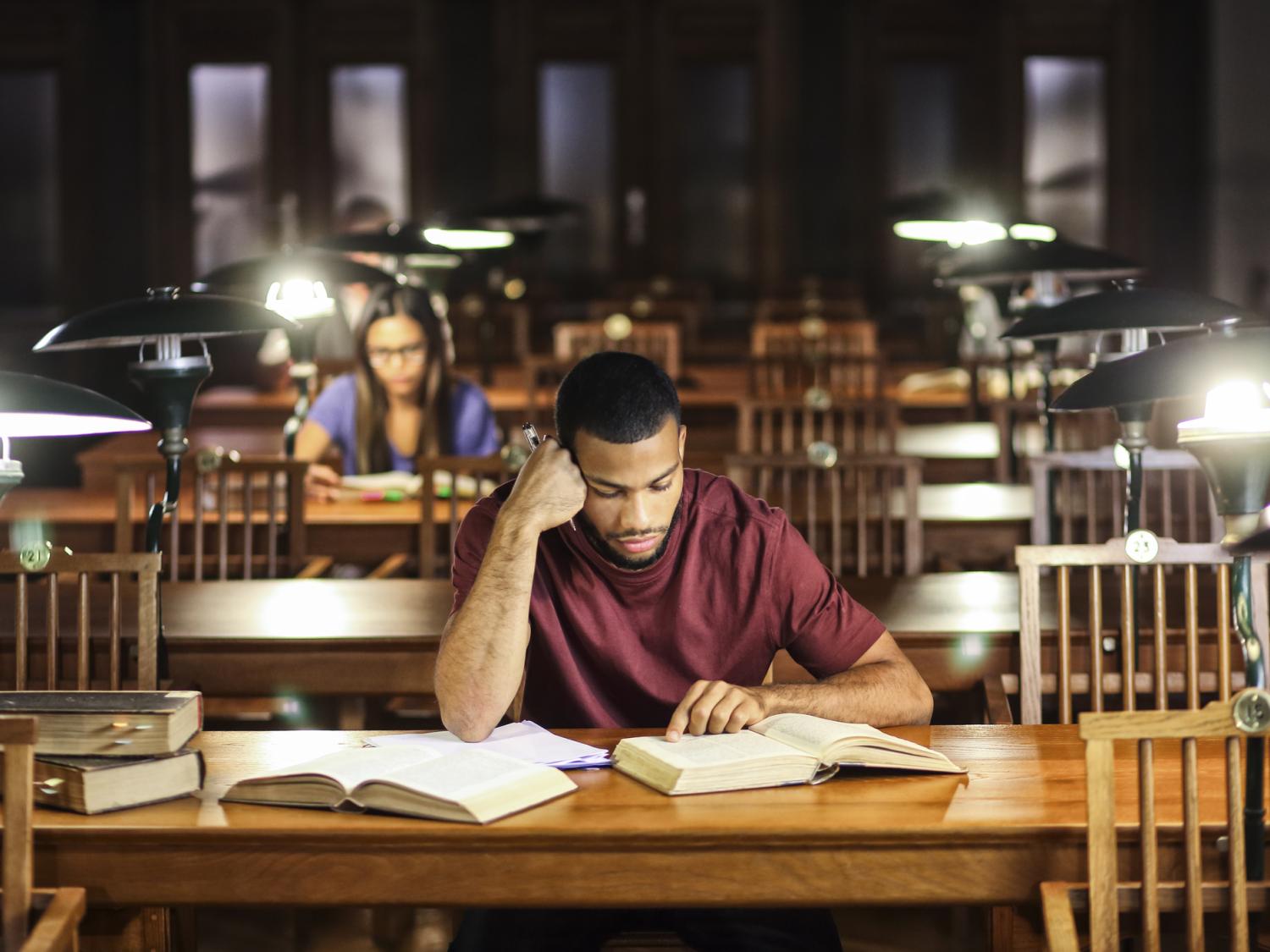 A Black student sitting with one elbow on the table studying