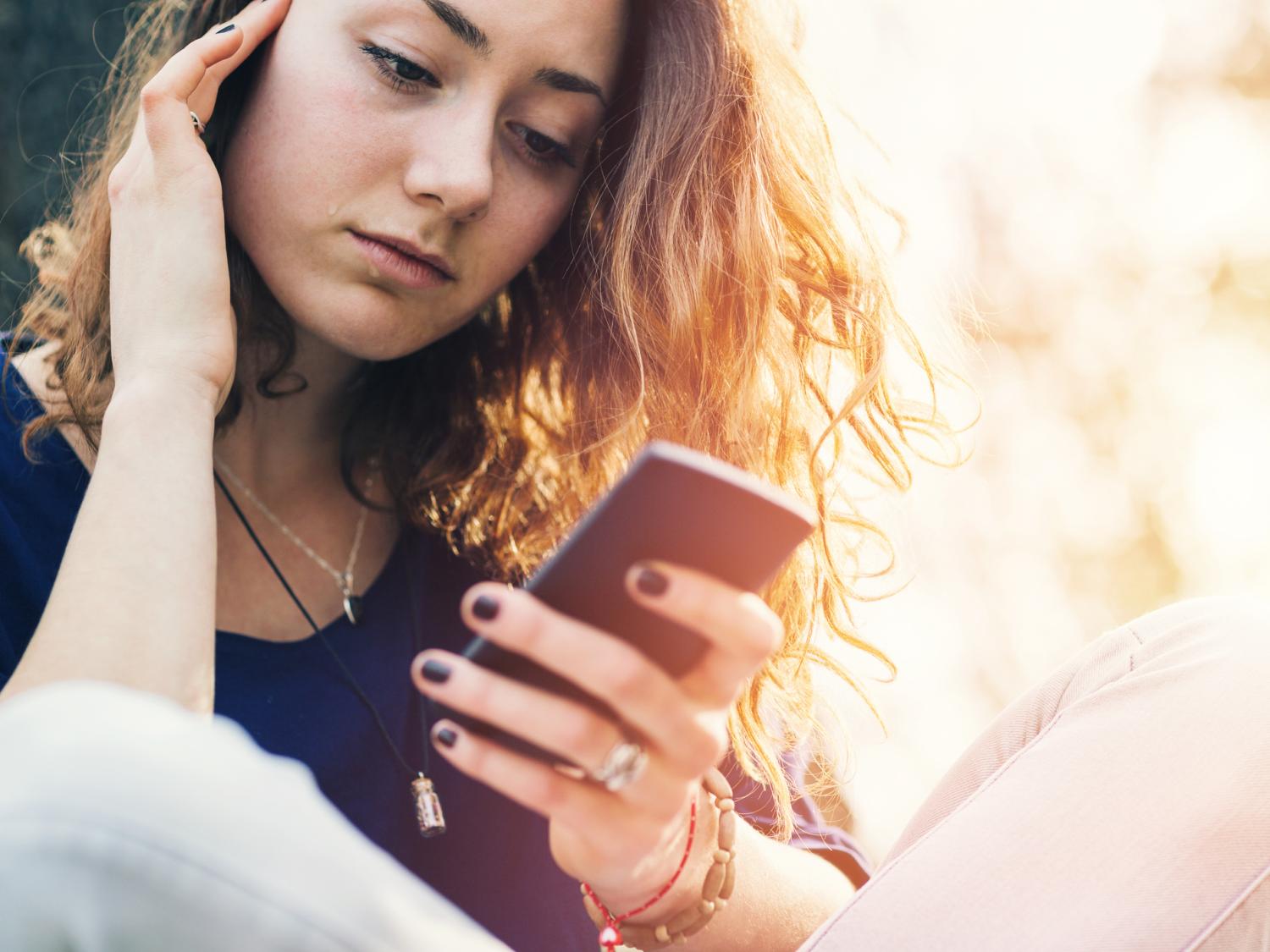 A teen holding her cheek while looking at her phone