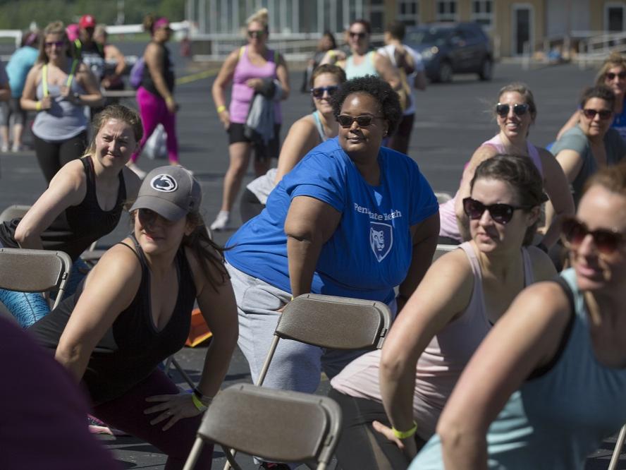 Meghan Culpepper, wearing sunglasses and a Penn State Health T-shirt, joins a group of women all in the same workout position staring at something to the left of the frame.