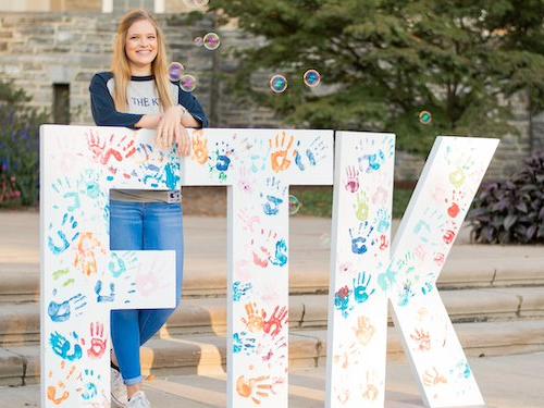 Young woman standing with large white letters "FTK" with colorful handprints on letters