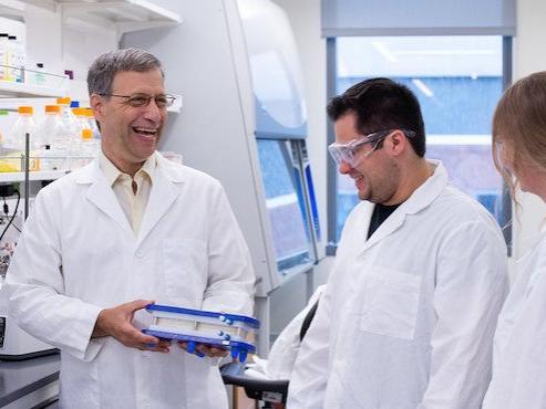 Two men and one woman in white lab coats working and laughing in lab