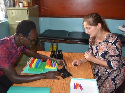 A Caucasian undergraduate student and a Kenyan man work with a 3D-printed peg board.