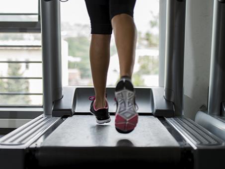 A runner’s legs on a treadmill. The runner is wearing sneakers.