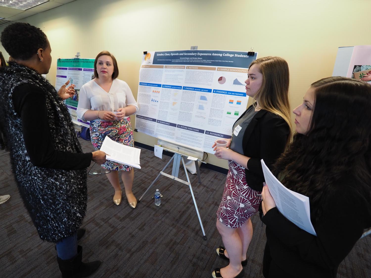 One woman asking three female students about their poster displaying their research