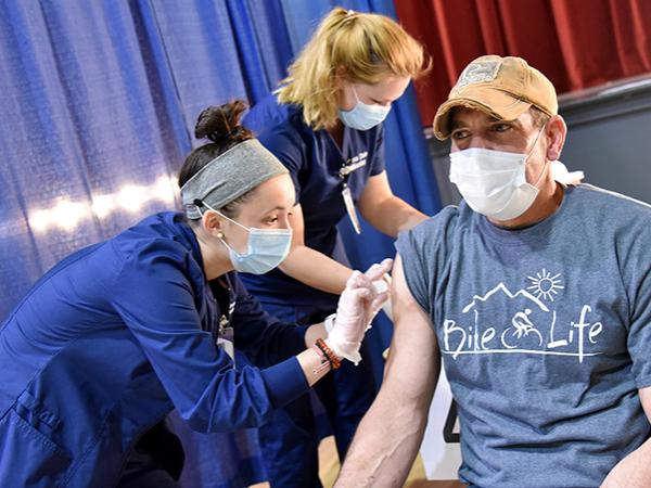Alex Higgins (front) and Sarah Schwarm (back) administer a covid vaccine to a community member.