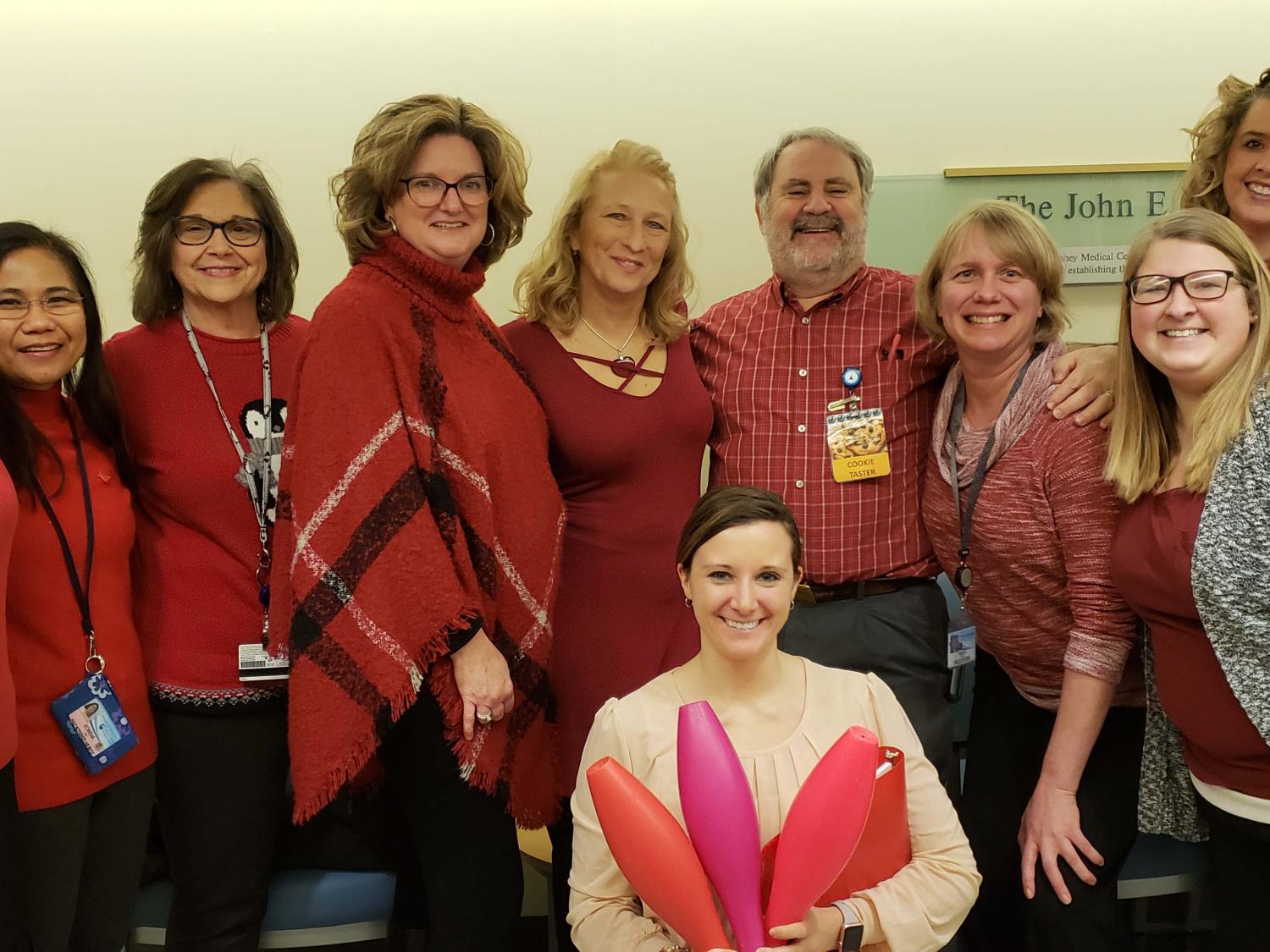 Members of the Pediatric Oncology team at Penn State Children’s Hospital stand in a semi-circle. One woman kneels, holding in her arms a collection of bowling pins. The team is participating in in National Wear Red Day.