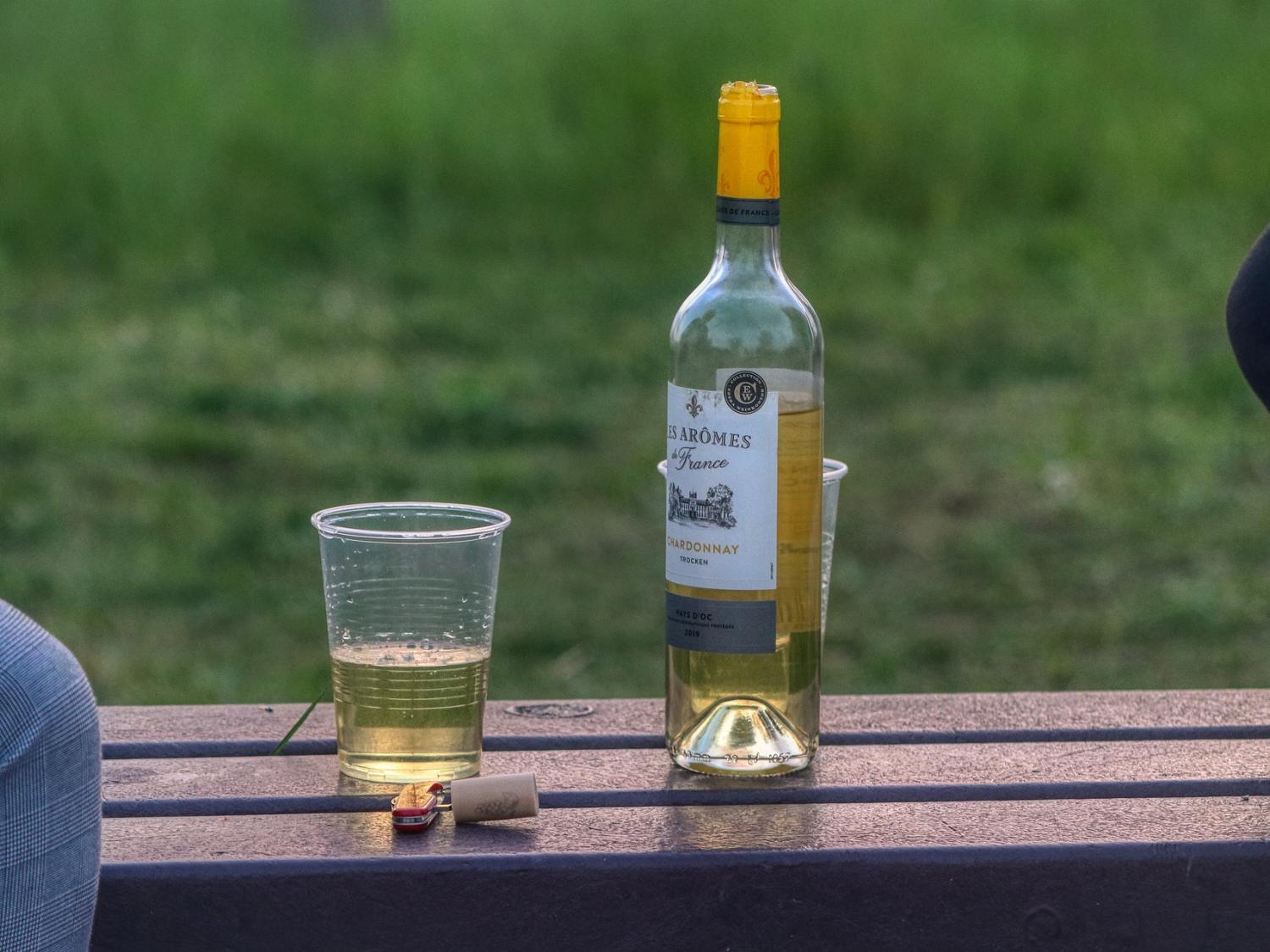 cup of wine next to wine bottle on bench
