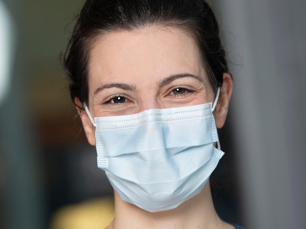 A closeup of a woman in a facemask, smiling.
