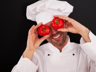 smiling cheff holding whole tomatoes in front of his eyes