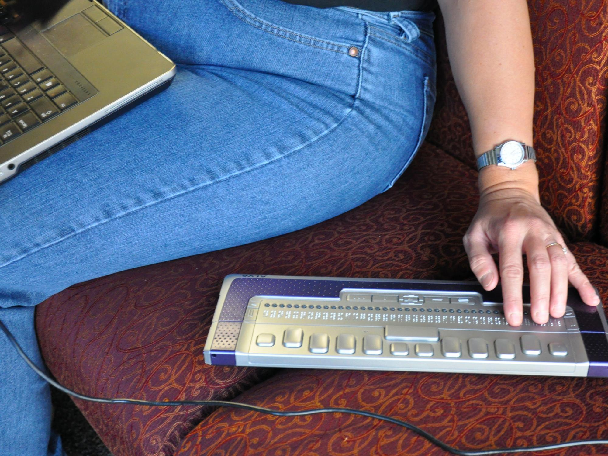A woman sits on a cough with her hand on a braille keyboard