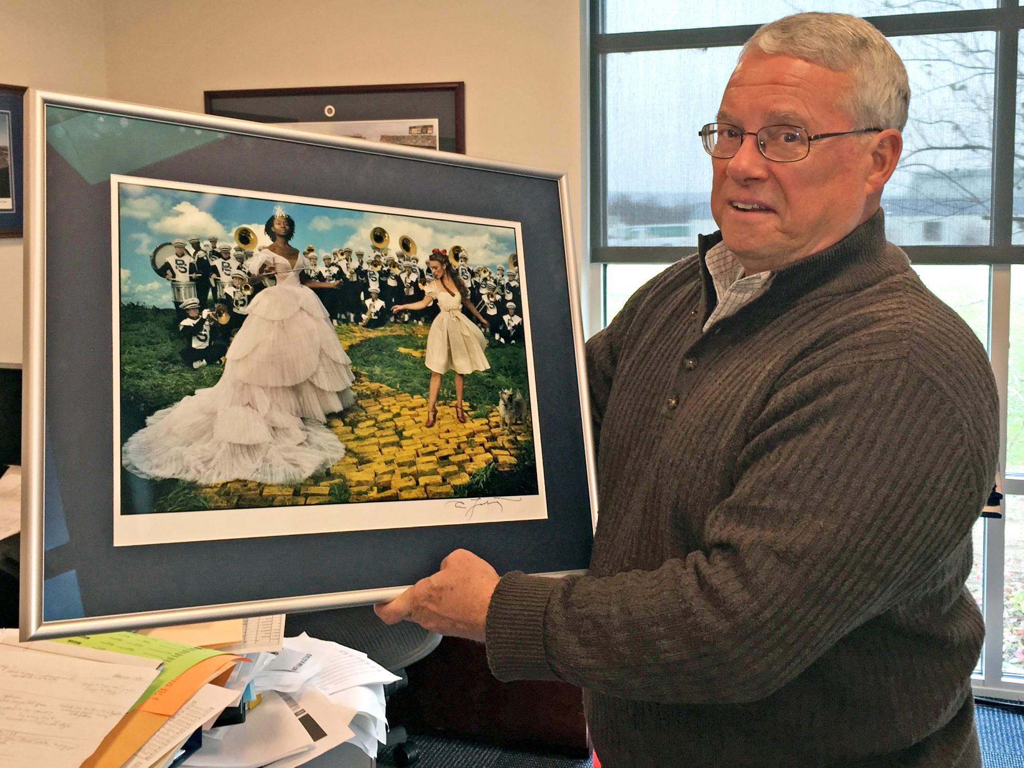 The Blue Band director holds up an Annie Liebovitz print featuring members of the Blue Band in the background.
