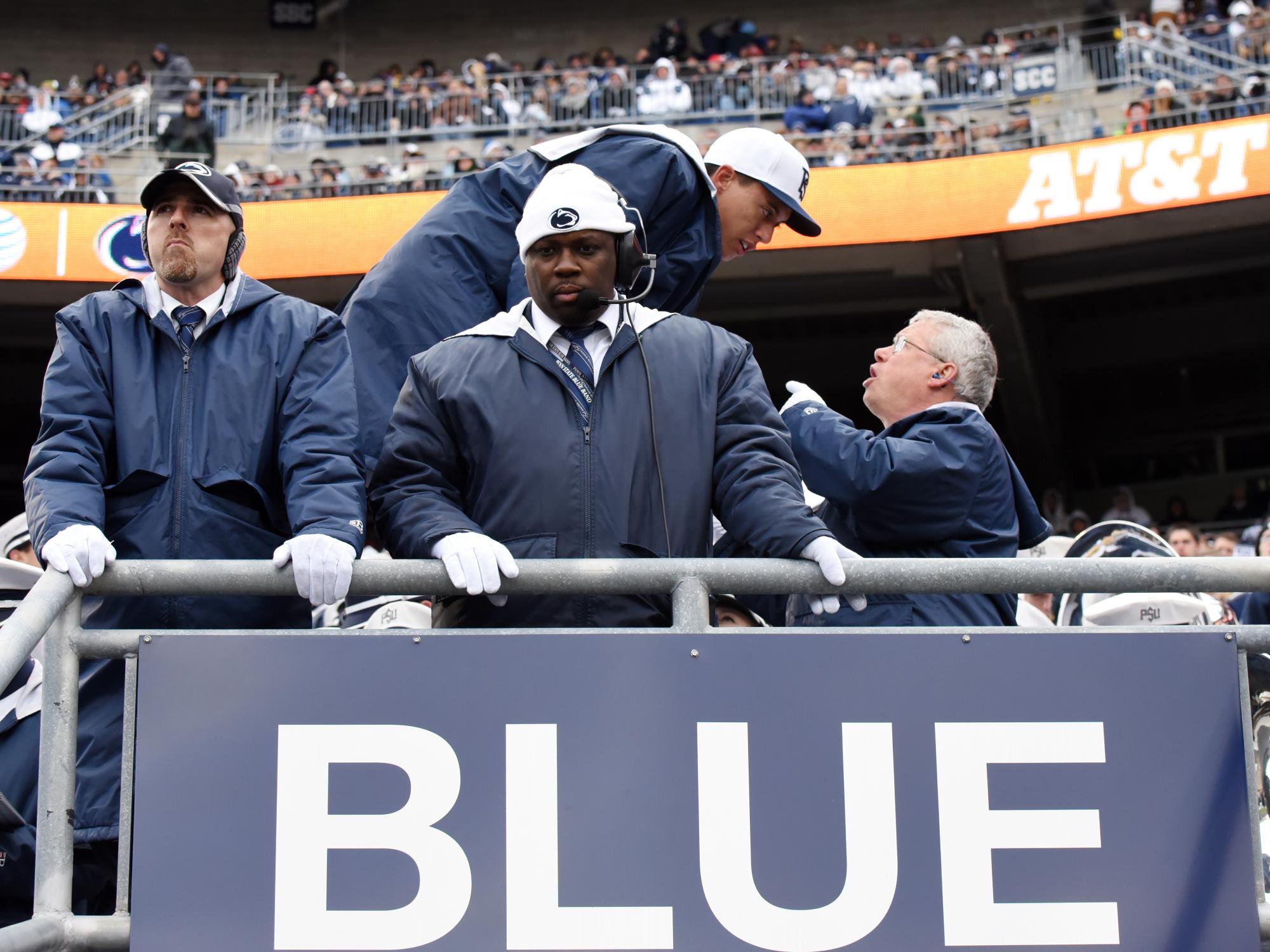 Dr. Bundy gives some instructions to the drum major in the background while, in the foreground, assistant directors keep an eye on the football game.