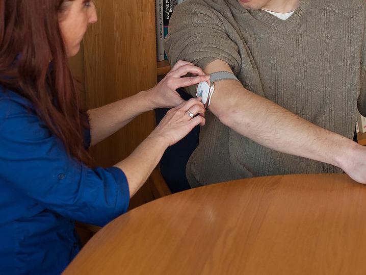 A woman adjusts a wearable sensor on a subject's arm