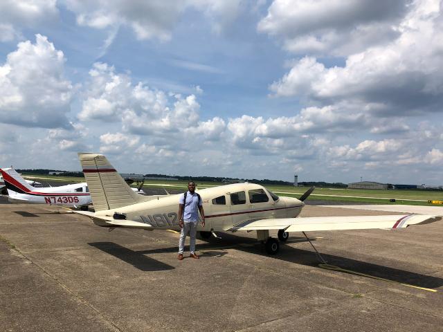 Newly-licensed pilot Trevor Baptiste stands outside an airplane.