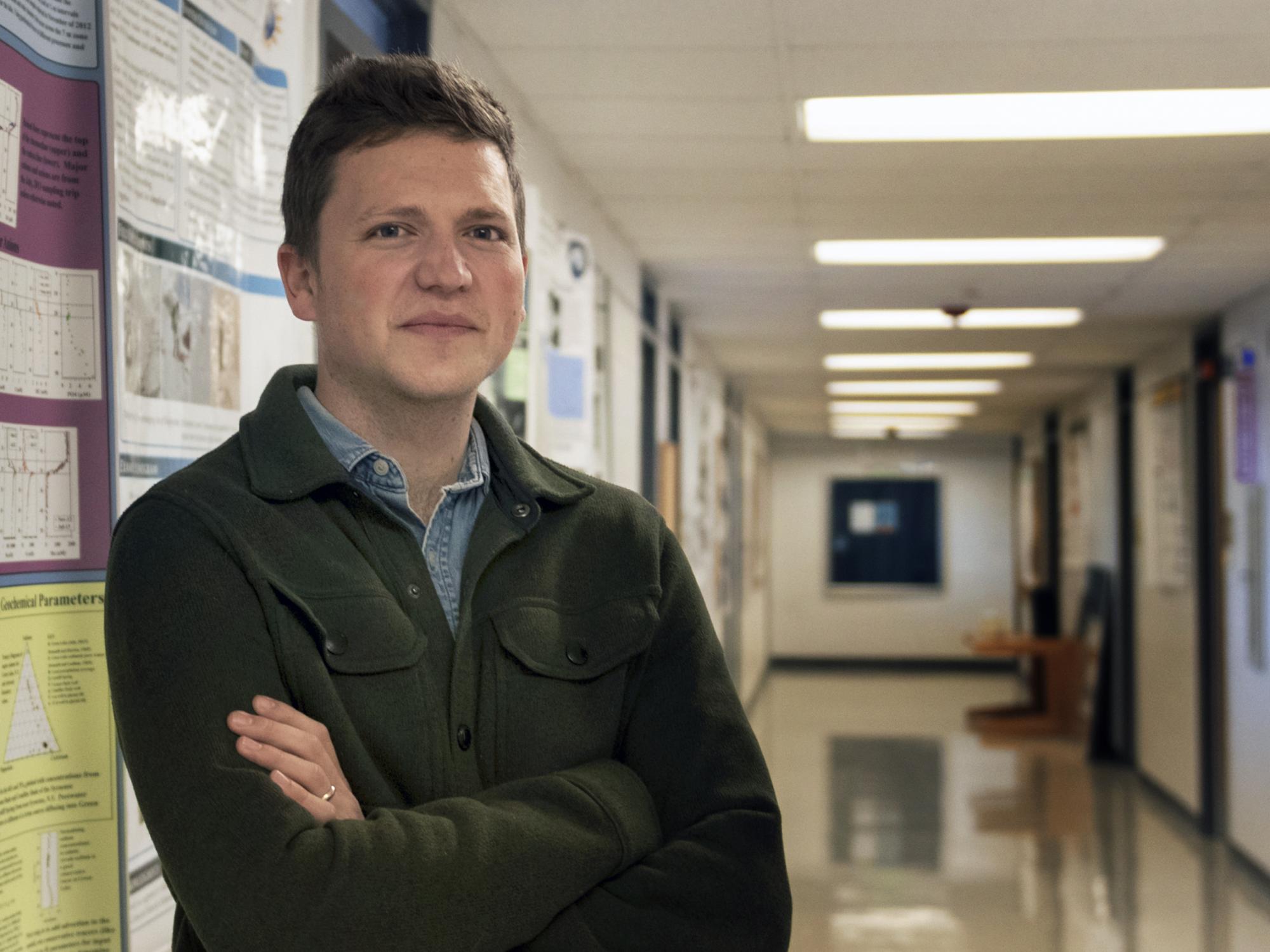 Max Lloyd standing and leaning against a wall in a hall on campus