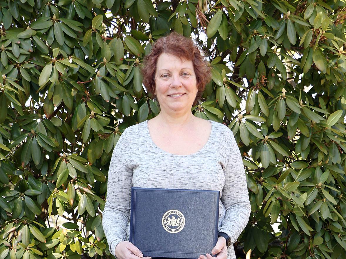 Woman holding plaque and standing behind black wooden rocking chair.