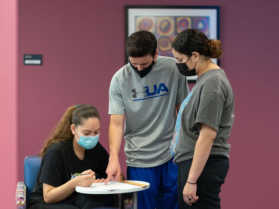 Students in masks looking at coursework on a desk.
