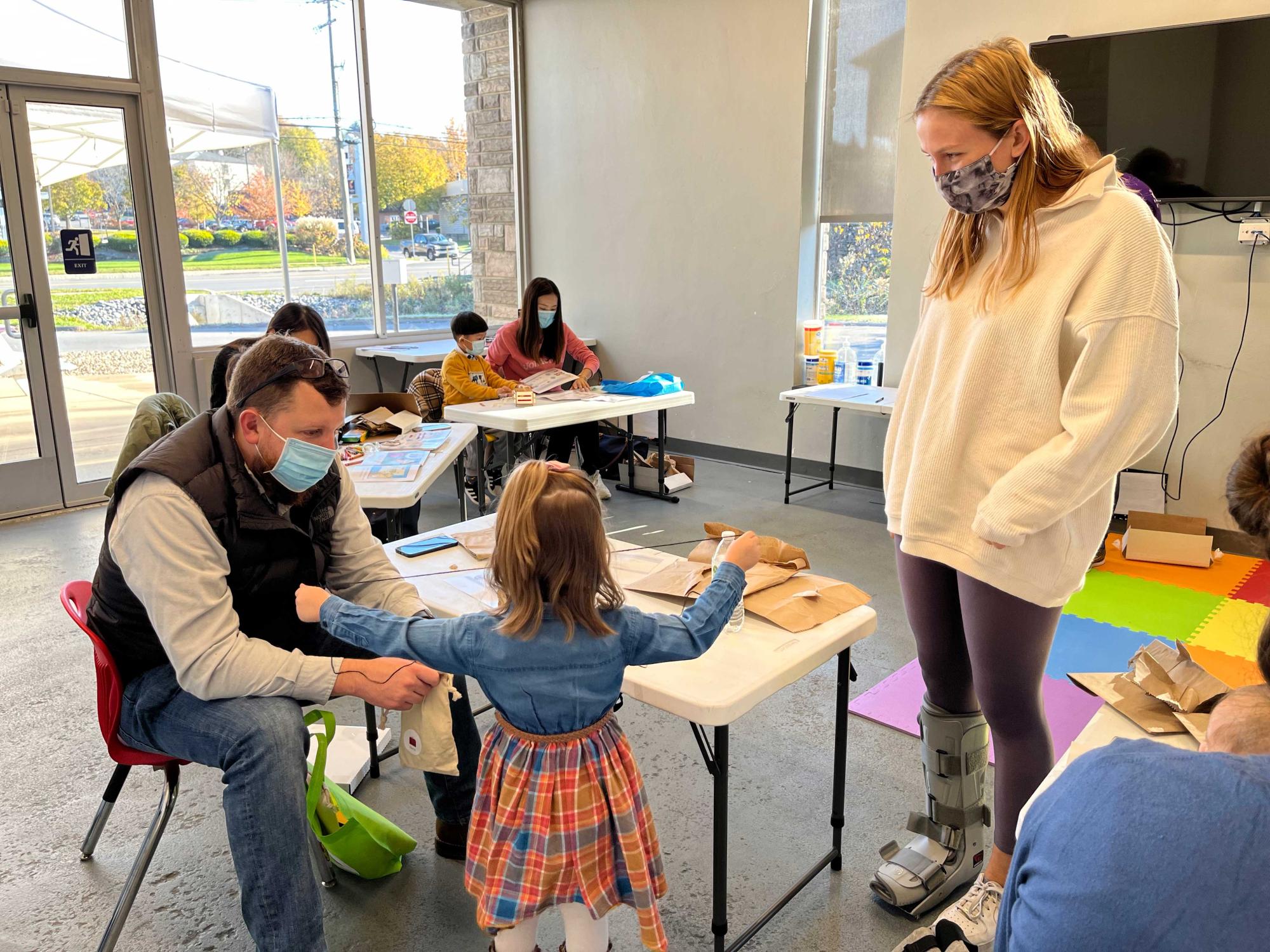 College student looks on as father and young daughter build a wagon together