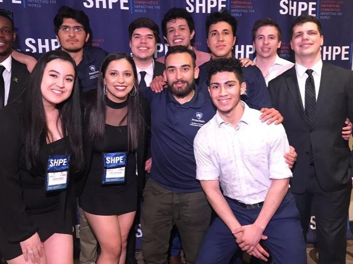 A group of students in the Penn State Society of Hispanic Professional Engineers pose in front of a branded backdrop.