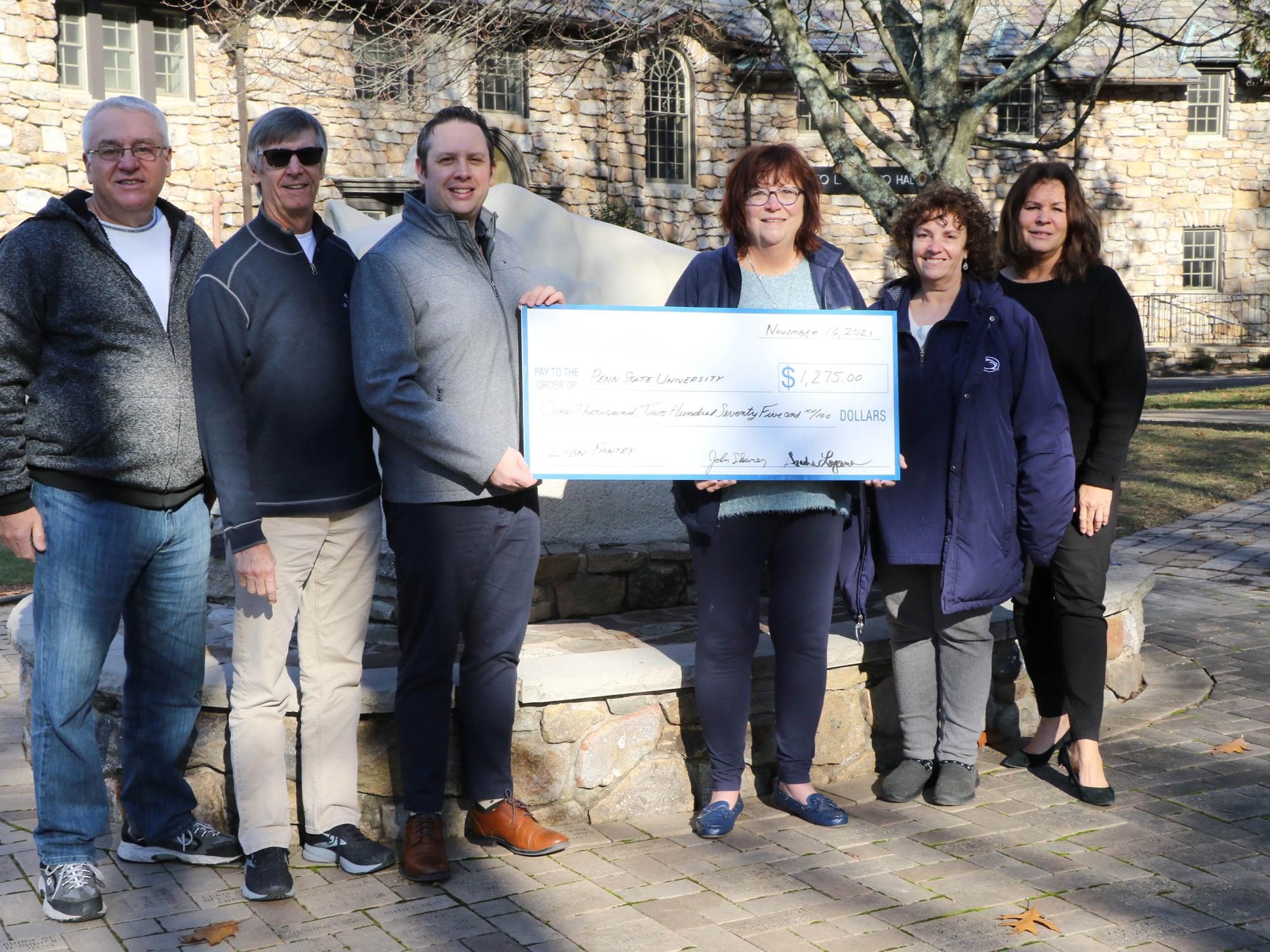 Group of men and women lined up in front of Nittany Lion statue holding large white check.