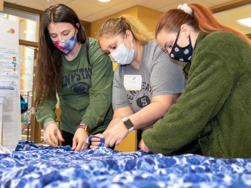 Three students knot ends of blanket