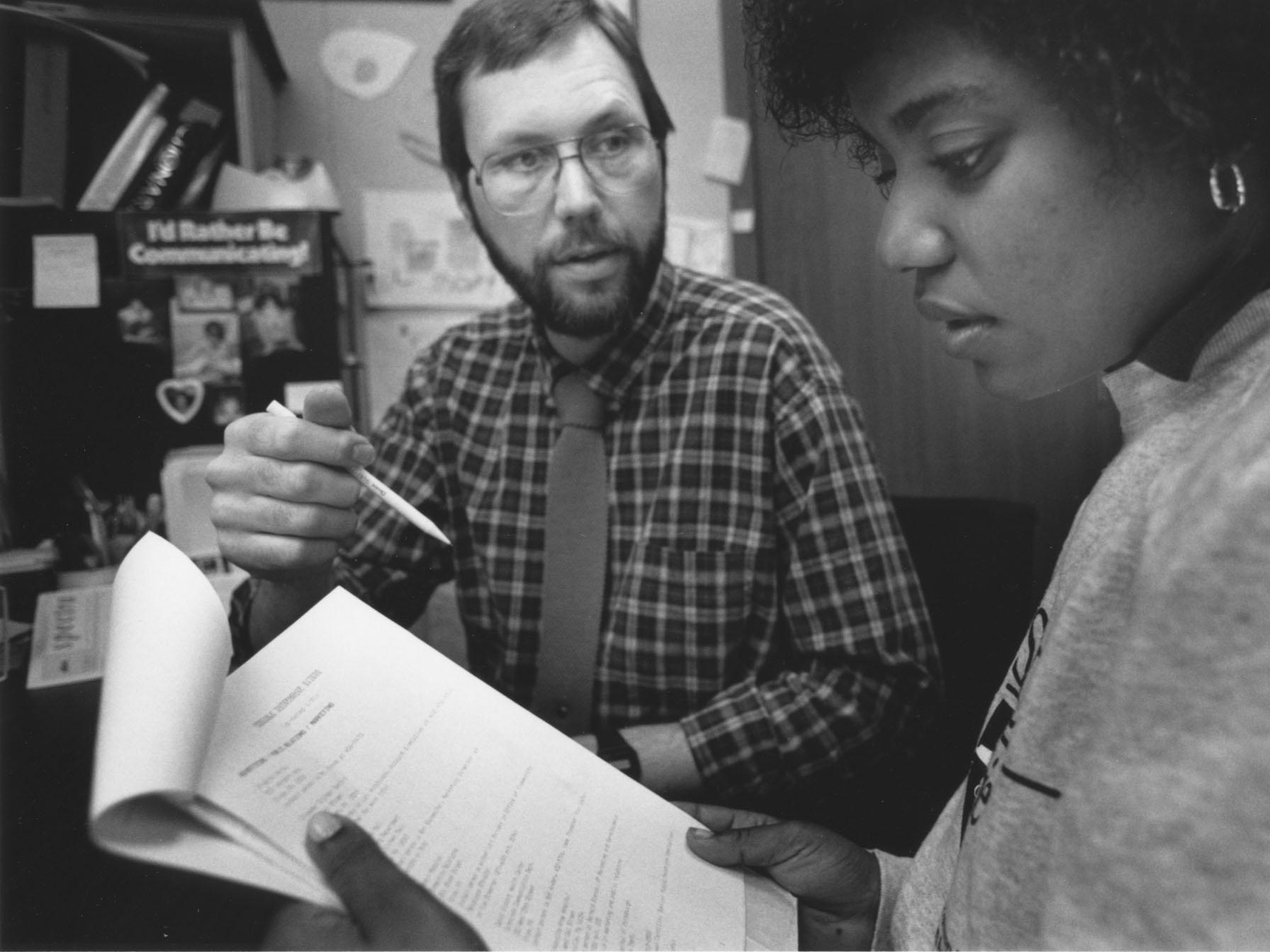 A black-and-white photo of Rod Troester, associate professor emeritus of speech communication, in an office with a student.