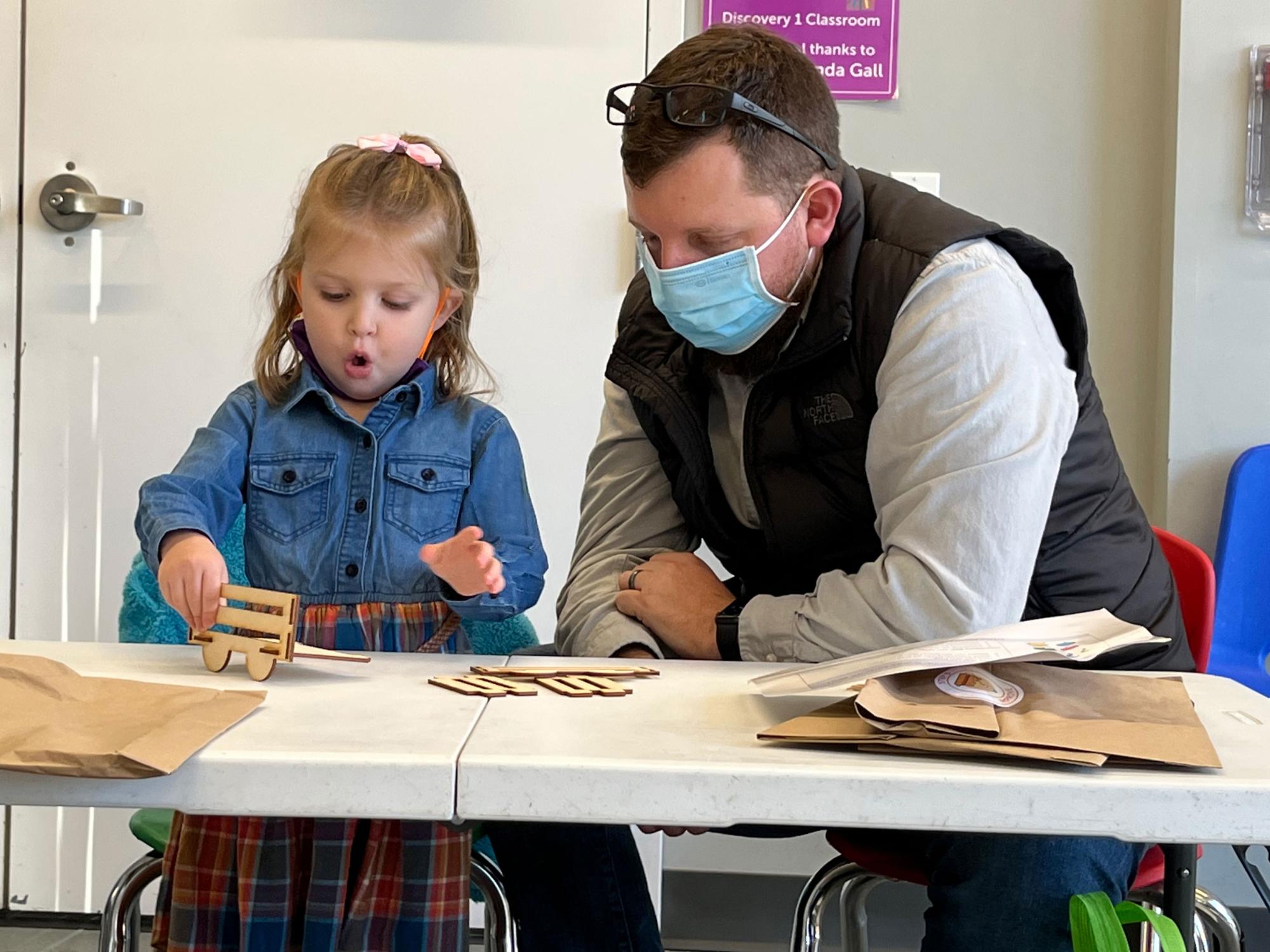 Father watches as her young daughter builds a toy wagon