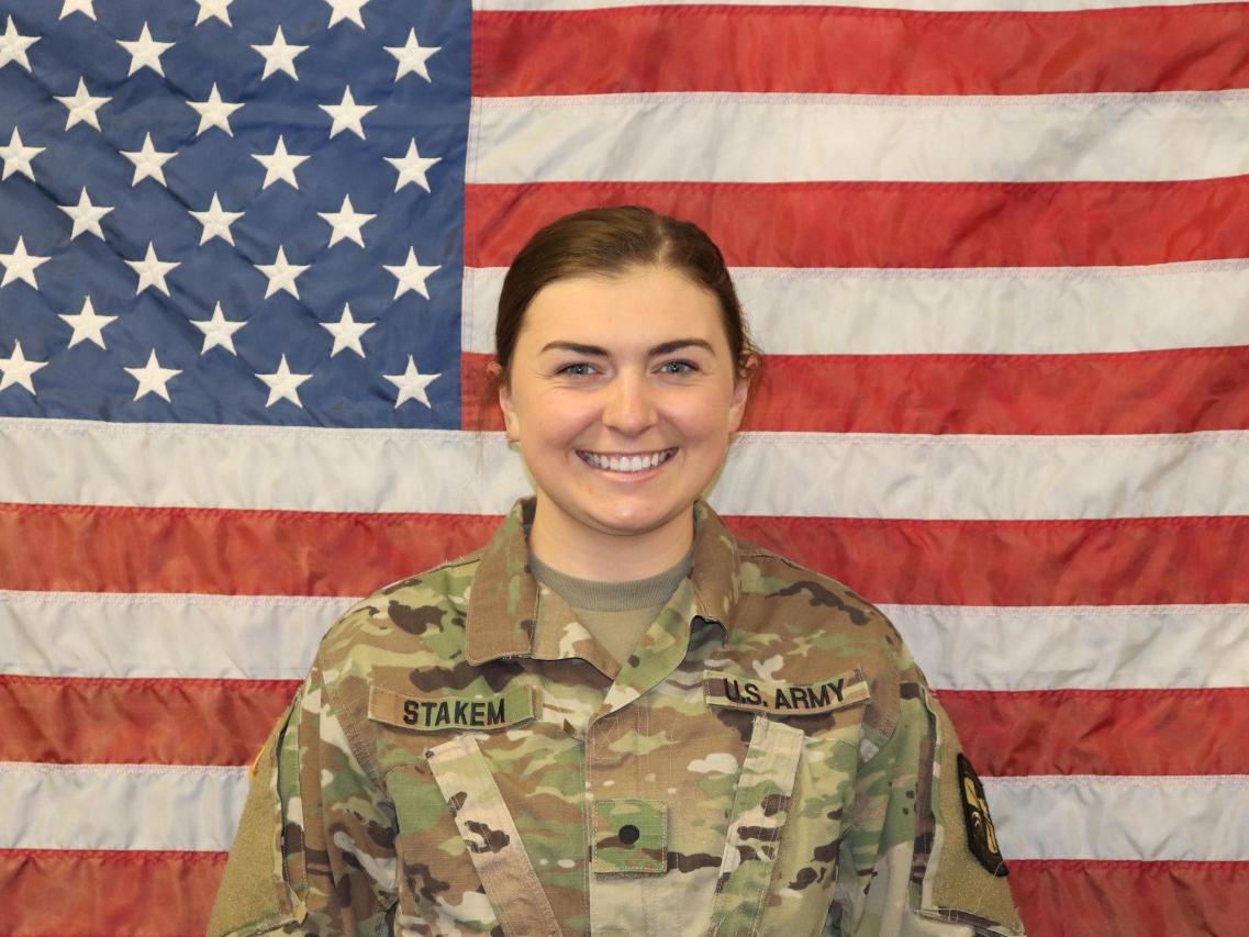 Young female service member smiles for photo in front of American flag.