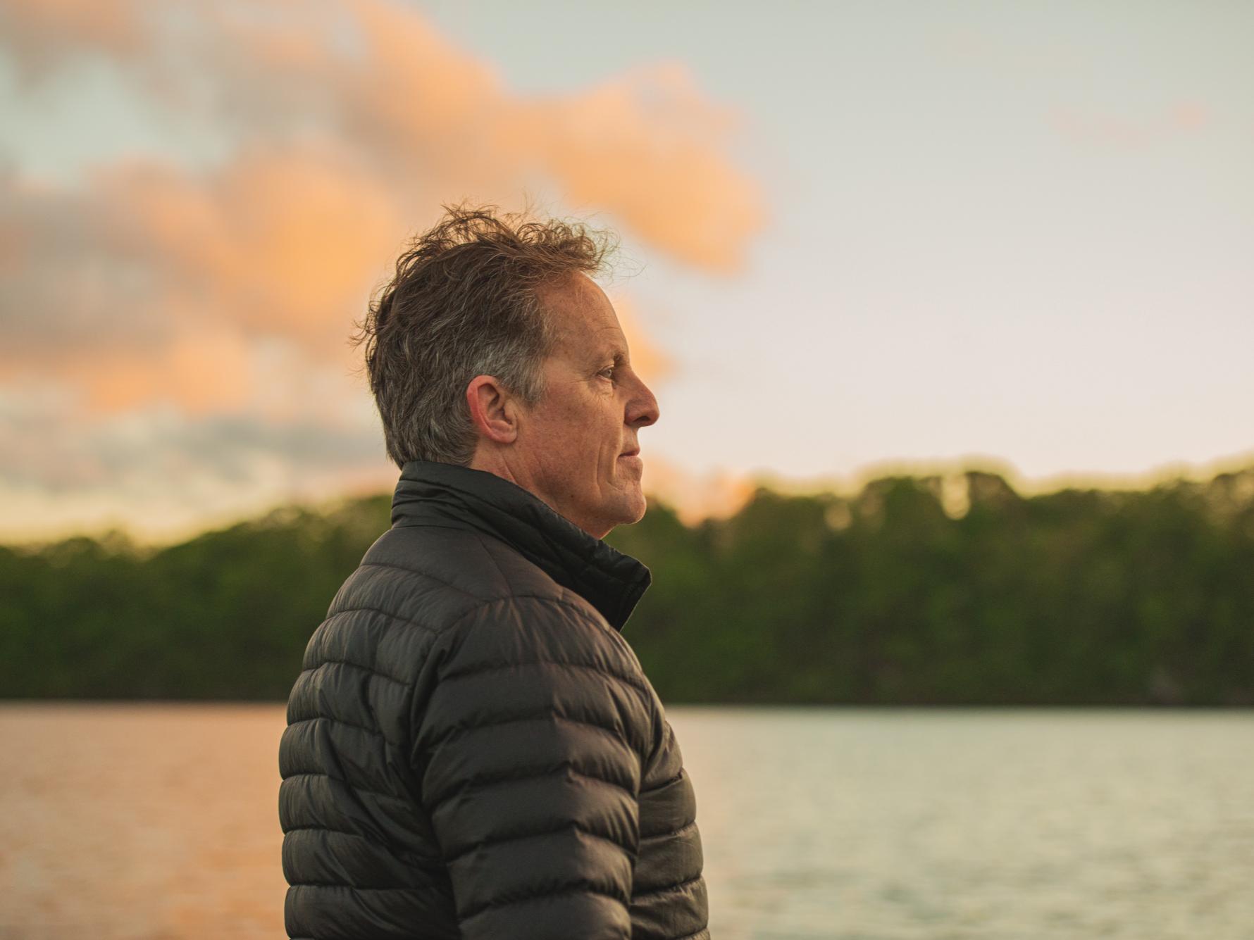 Lee Kump, the John Leone Dean in the College of Earth and Mineral Sciences, stands by a lakeside and looks across the waters to the trees lining the other side.
