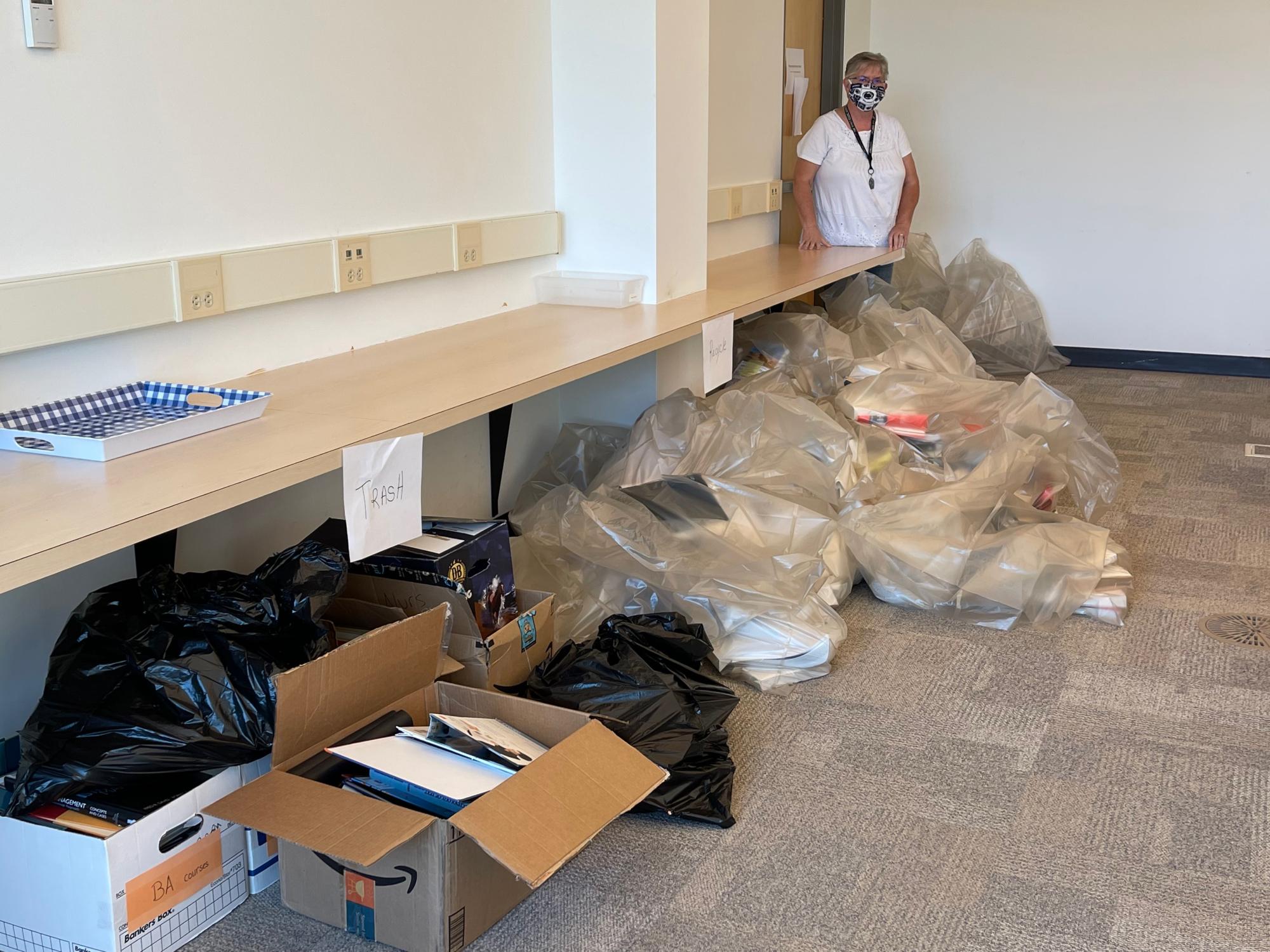 Kathy Highbaugh, Manager of Quality Assurance at World Campus Learning Design, stands next to the books amidst the recycling process.
