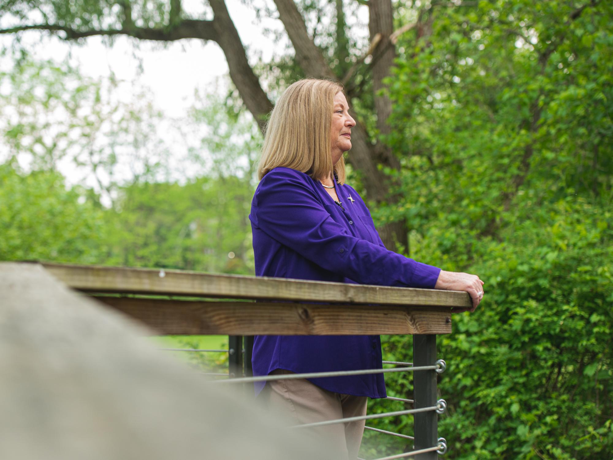Laurie Badzek, dean of the Nese College of Nursing, stands on a walkway in a wooded area, looking thoughtfully at the nature surrounding her.