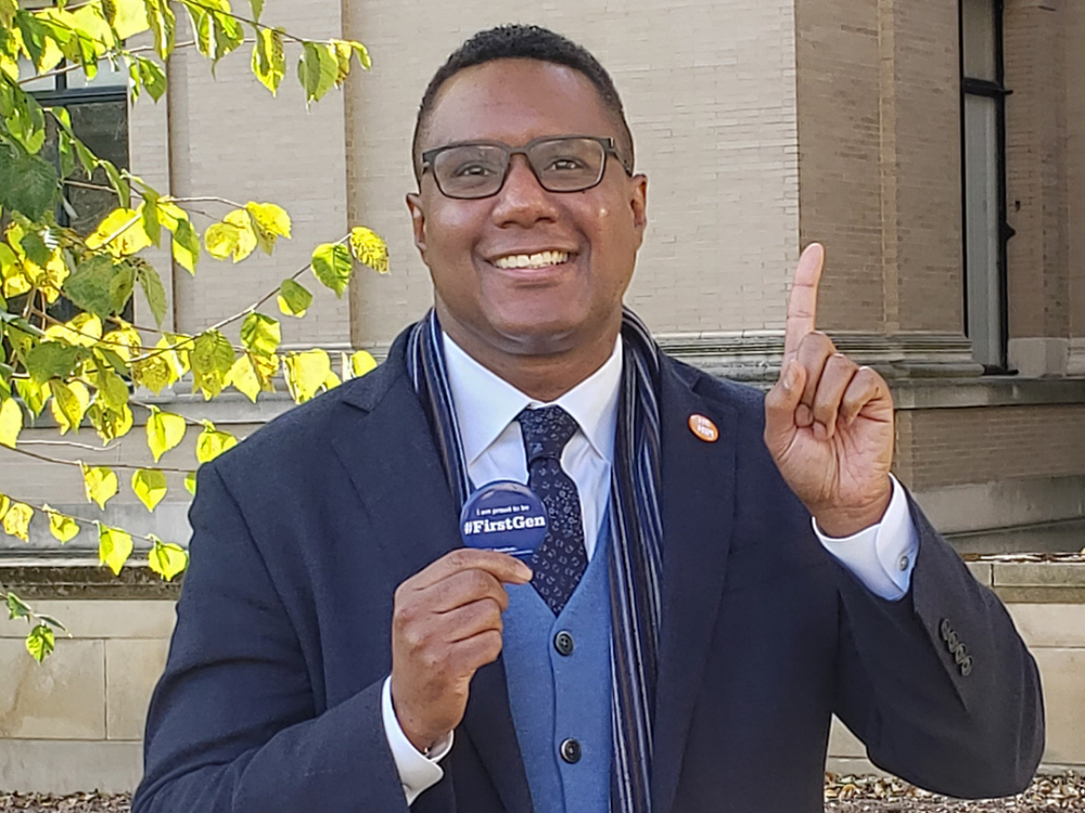Clarence Lang holds a button and holds up one finger while smiling at the camera