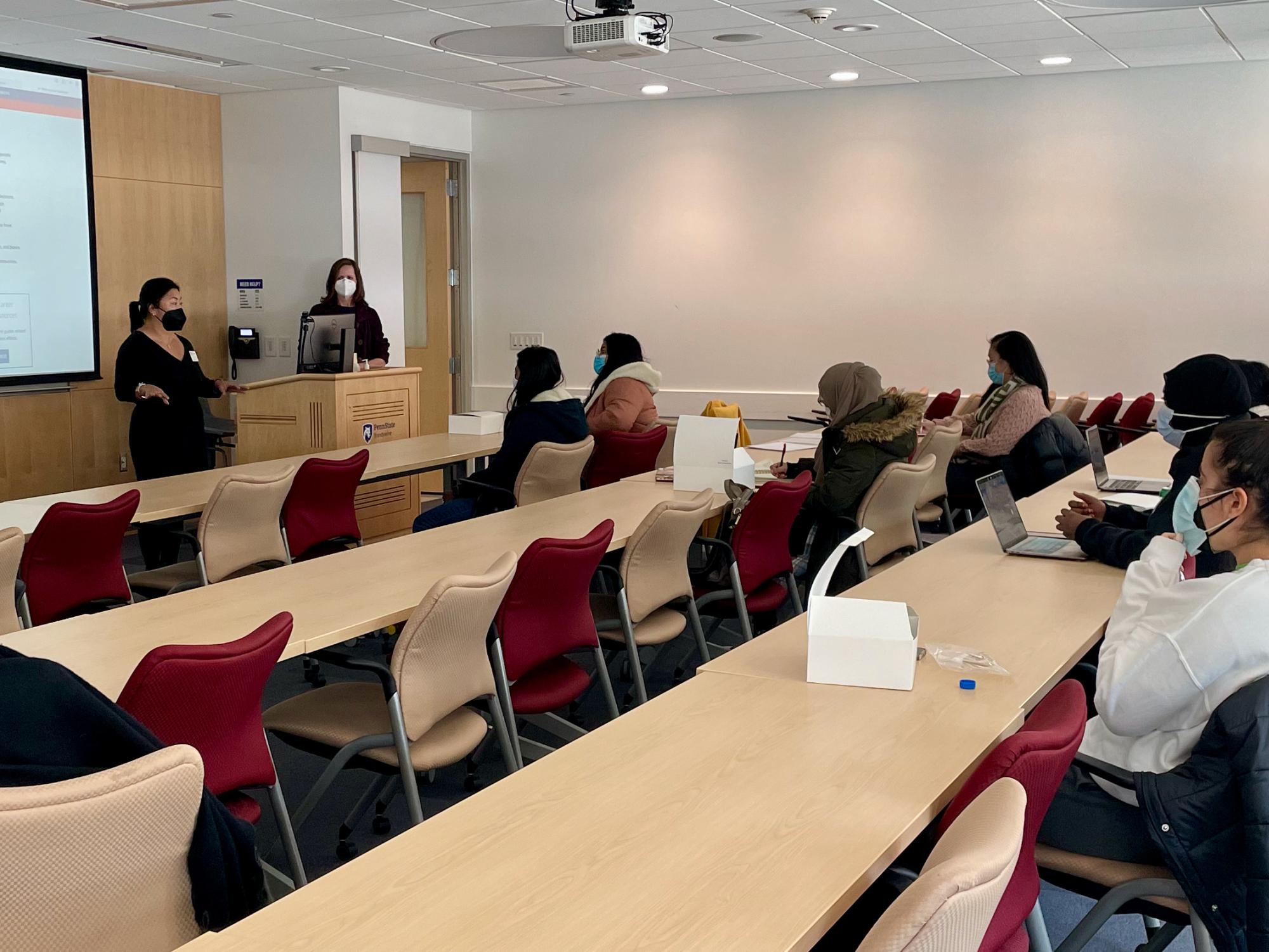 Students sit at desks in red chairs engaging with a speaker during a workshop on identity and values. 