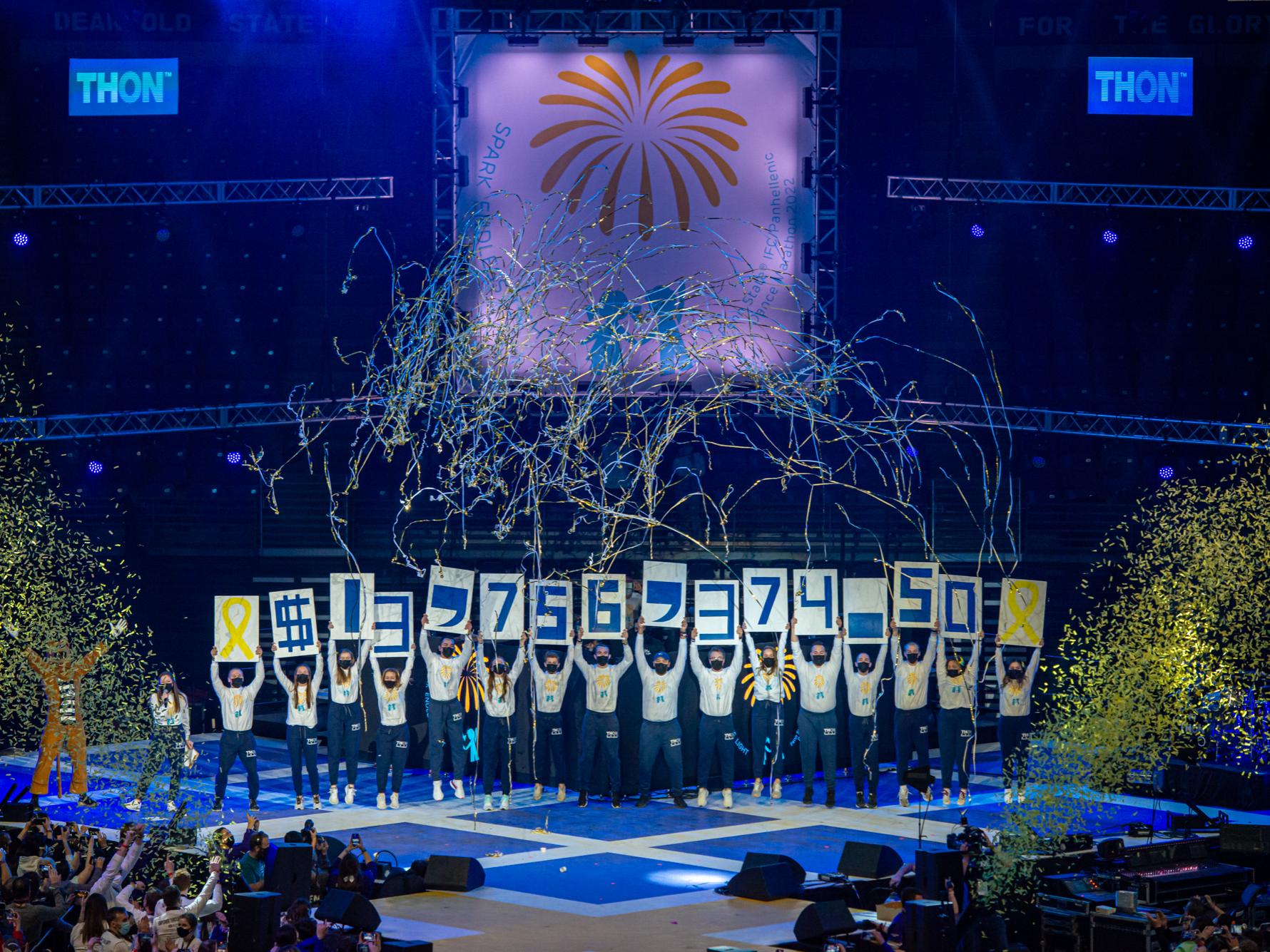 Penn State students celebrate on an arena stage, holding signs revealing the total raised during THON 2022: $13,756,374.50